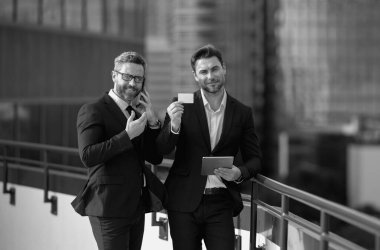 Çevrimiçi para işlemleri, mobil ödemeler. Takım elbiseli iki iş adamı dışarıda kredi kartı ve laptop tableti tutuyor. Hesabı öde. Şehirde kredi kartı olan bir adam. Finansal büyüme, çevrimiçi iş