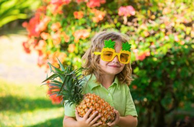 Ananas tutan ve dışarıda gülümseyen genç bir çocuk.