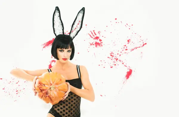 stock image Pretty woman clothed in dress rabbit with pumpkins. Sexy zombie girl holding a pumpkin on white bloody Background. Halloween make-up beautiful woman