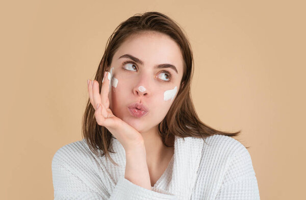 Funny beautiful woman applying moisturizer cream on her pretty face. Female skin care, close up face beauty portrait