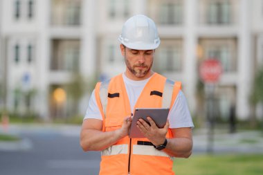 Tabletli mühendis, bina teftişi. İnşaat alanındaki bir inşaatçının portresi. İnşaatçı yeni bir ev inşa etmeye hazır. İnşaatçılar bina üniforması ve miğfer giyerler.