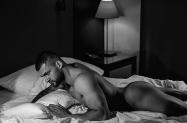 Handsome nude man lying in a bed. Top view of handsome young man in bed in bedroom at night. Muscular handsome man laying on stomach in bed. Guy lying on belly and covered sexy body by blanket
