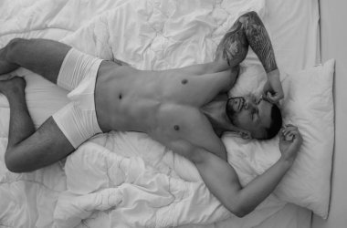 Top view of sexy guy in bedroom. Young handsome man in bedroom. Shirtless sexy male model lying on bed in his bedroom. Body portrait of a nude male model in bed. Dreaming guy enjoying night