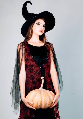 Cadı kostümlü göz kamaştırıcı vampir. Balkabağıyla poz veren kadın. Cadıların şapkası ve kostümü içinde balkabağı tutan genç ve güzel bir kadın.