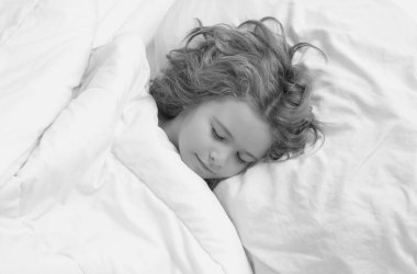 Çocuk rahat beyaz bir yatakta uyuyor. Sarışın, beyaz bir çocuğun güzel yüzü, yatakta uyuyor. Tatlı rüyalar. Küçük bebek evde yatarken uyuyor.