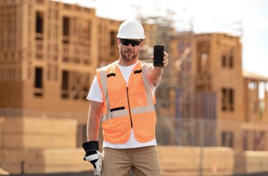 İşçi telefonu, inşaatçı telefon ekranı. Cep telefonu olan bir mimar. Kasklı inşaat işçisi dışarıda çalışıyor. İnşaatta güvenlik kasketi takmış bir inşaatçı.