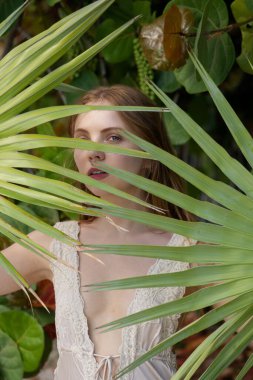 Yeşil palmiye yaprağıyla kadın yüzünü kapat. Cilt bakımı güzellik tedavisi konsepti. Temiz, sağlıklı bir cildi olan bir model. Doğal makyajlı güzel bir kadın bir palmiye yaprağı tutuyor. Kaplıca ve