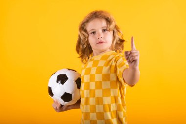 Çocuk çocuk klasik futbol topunu sarı stüdyoda izole bir şekilde tutuyor. Stüdyoda elinde futbol topu tutan çocuk. Çocuk topla oynuyor. Spor, çocuklar için futbol hobisi. Futbol topuyla poz veren küçük bir futbolcu