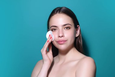 Removing makeup with cotton pads. Cleaning face with pad. Cosmetic cotton pad. Young woman caring for facial skin using cotton pad in studio. Beauty care and pampering. Daily skincare