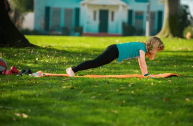 Child is pushing up on the green grass. Boy doing push-ups in the yard. Kid pushing up