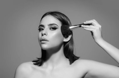 Kızarık allık tutan kız stüdyo arka planında izole edilmiş toz pudrası uyguluyor. Yanaklarını pudralayan genç bir kadın. Makyaj fırçası. Kadın modelin elmacık kemikleri kızarır.