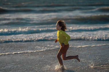 Çocuk yaz tatilinde sahilde koşuyor ve eğleniyor. Denizde oynayan mutlu çocuklar. Doğada denizli çocuklar. Deniz kıyısında tatilde deniz suyunda koşan mutlu çocuklar. Çocuk deniz sahilinde yürüyor.