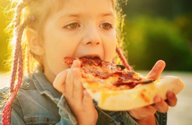 Çocukların en sevdiği yemek. Lezzetli pizza. Çocuk pizza yiyor. Fastfood. İtalyan abur cuburu. Küçük kız dışarıda öğle yemeği.