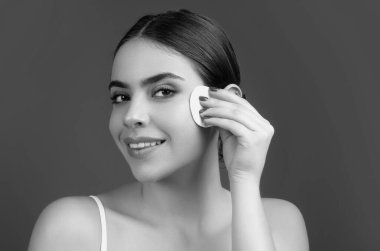 Beautiful young woman with cotton pad removing makeup. Skin care. Studio portrait of girl cleaning her face with cotton pad, isolated beige background. Face toner and cotton pad