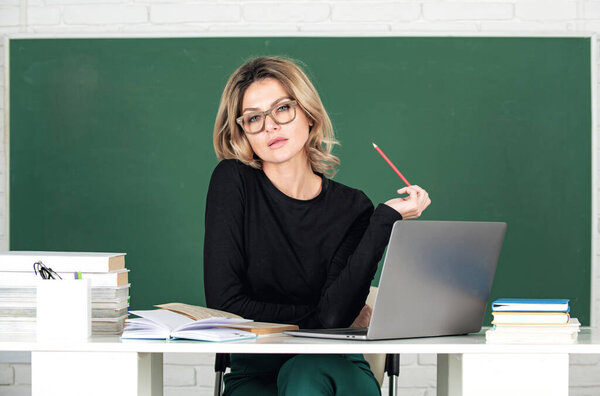 Portrait of beautiful teacher or female tutor working at table in college or high school. Young women student studying in class