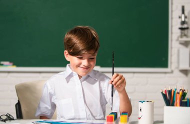 Resim ödevi yapan, elinde kalem tutan, yazı yazan okul çocuğu. Çocuk ilkokulda resim çiziyor. Çocukluk eğitimi, çocukların sanatsal becerileri.