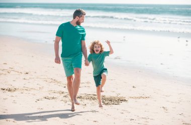 Baba ve oğul yaz plajında koşuyor. Baba ve çocuk dışarıda oynuyorlar.
