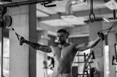 Muscular men lifting weights. Powerful male fit model doing workout in gym. Man lifting dumbells, strong athletic fit man doing exercises with dumbbells. Weightlifting workout. Fitness workout