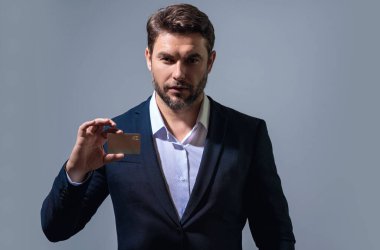 Gri arka planda kredi kartı olan bir adamın stüdyo portresi. Para yönetimi ve kredi puanı. Ödül parası. Kredi limiti. İnternetten alışveriş konsepti. Kredi geçmişi. Finansal sorumluluk