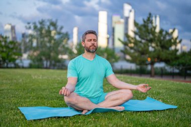 40 'lı yaşlarda bir adam şehir parkında temiz hava soluyor. Nilüfer pozisyonunda otururken yoga ya da meditasyon eğitimi alan bir adam. Nefes alma ve denge. Parkta meditasyon yapan bir adam. Sağlıklı yaşam tarzı