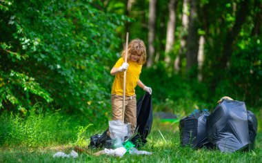 Çocuk parkı temizliyor, çöpü çöp torbasına koyuyor. Çevresel koruma. Çocuk temizlik için çöp poşeti topluyor. Çöpler için siyah torbada çöp bulundurmak. Kirlilik ve geri dönüşüm