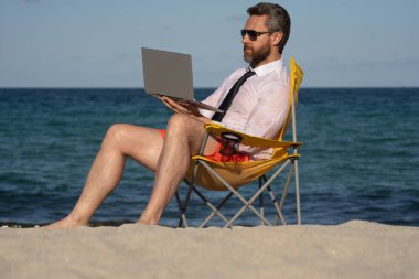 Deniz sahilinde dizüstü bilgisayar kullanan iş adamı. Yaz tatilindeki çılgın iş adamı. Heyecanlı iş adamı, çılgın komedi dünyası konsepti. Uzaktan kumanda çalışıyor. Yaz iş hayalleri