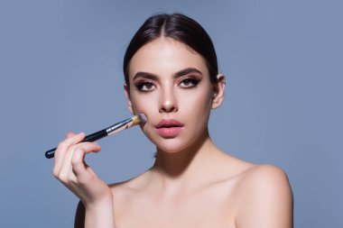 Beautiful woman applying makeup holding brush. Beauty make up concept of an young woman. Beauty salon. Skin care and natural makeup. Girl gets blush on the cheekbones. Beauty care and treatment