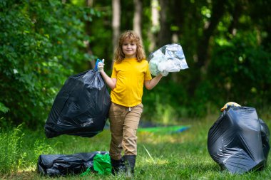 Çöp poşeti dolusu çöp ve çöp maşası olan bir çocuk. Geri dönüşüm kutusuyla ormanda veya parkta plastik atık toplayan sevimli bir çocuk. Çevre aktivistleri. Çevresel koruma ve ekoloji