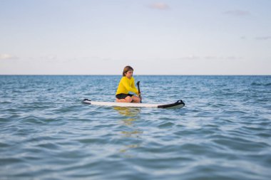 Mutlu çocuk yaz denizinde oynuyor. Karayip Denizi 'nde turkuaz güzel bir göl ve sağlıklı bir yaz tatili aktivitesiyle ayakta kürek çekmekten hoşlanan bir çocuk. Çocuk SUP sürüyor. SUP yönetim kurulundaki yaz çocukları