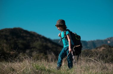 Sırt çantalı küçük bir çocuk manzaralı dağlarda yürüyüş yapıyor. Çocuk yerel bir turist yerel bir yürüyüşe çıkıyor.