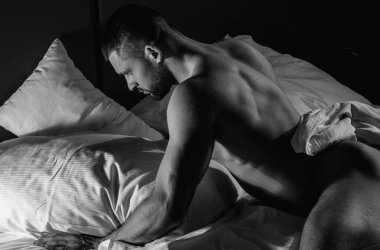 Handsome nude man lying in a bed. Top view of handsome young man in bed in bedroom at night. Muscular handsome man laying on stomach in bed. Guy lying on belly and covered sexy body by blanket