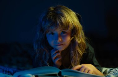 Yatakta uzanmış kitap okuyan sevimli bir çocuk. Uyku masalı, çocuk masalı.