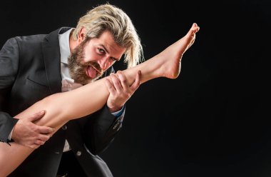 Takım elbiseli, kadın bacaklı bir erkek. Ayak fetişi olan adam bacağını yalıyor. Lüks ve ataerkil