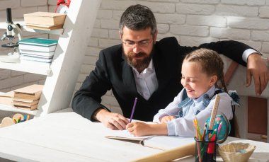 Öğrenci kız, öğretmeniyle birlikte ders çalışıyor ve yazı yazıyor. Sevimli öğrenci kız okul malzemeleriyle masasının yanında gülen yüz ifadesiyle ders çalışıyor.