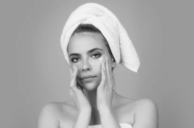 Göz bandı. Göz altlarında kolajen pedleri olan güzel kadın yüzü. Stüdyo çekimlerinde genç bir kadının gözlerinin altına kolajen bantları yapıştırılmış taze ve sağlıklı bir derisi var. Kafasına havlu takıyor ve yüz bakımı yaptırıyor.