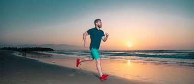 Yaz denizinde koşan sporcu bir koşucu. Sağlıklı yaşam tarzı kavramı. Açık hava antrenmanı sırasında günbatımı geçmişli formda bir erkek fitness koşucusu. Kopyalama alanı olan panorama
