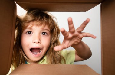 Çocuk karton kutunun içine bakıyor, alt manzara. Satın aldıklarınızı teslim ediyorum. Çocuklar doğum gününü kutlar. Doğum günü hediyesi. Çocuk açma paketi