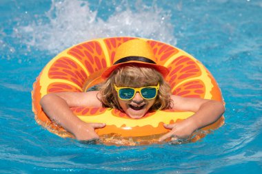 Havuzda yüzen çocuk yüzen yüzükle oynuyor. Güneş gözlüklü sevimli çocuk yaz günü havuzda şişirilebilir yüzüklerle yüzer.