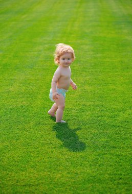 Yaz akşamında çimlerin üzerinde mutlu bir bebek. Dışarıda bebek bezi takan gülümseyen bir çocuk. Mutlu çocukluk ve çocuk sağlığı hizmetleri