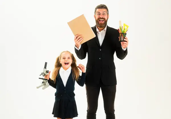 Stock image Cheerful smiling little girl in school uniform having fun. Fun kids education. Elementary amazed pupil with school supplies and excited teacher in studio, isolated on white background