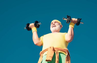 Kıdemli adam dambılı kaldırıyor. Yetmişli yaşlardaki kıdemli adam antrenman yapıyor ve ağırlık kaldırıyor. Kıdemli sporcu dambılları kaldırıyor. Yaşlı adam egzersizi.