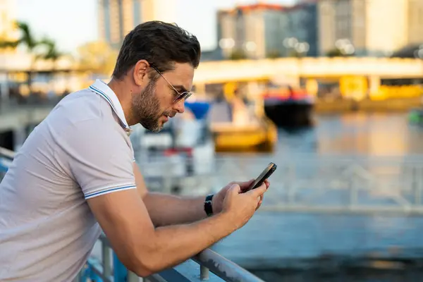 stock image Portrait of handsome male model chatting on phone outdoor. Stylish man talking on phone dressed in polo. Fashion male posing on the street background. Urban style. Business phone conversation