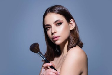 Beautiful woman applying makeup holding brush. Beauty make up concept of an young woman. Beauty salon. Skin care and natural makeup. Girl gets blush on the cheekbones. Beauty care and treatment