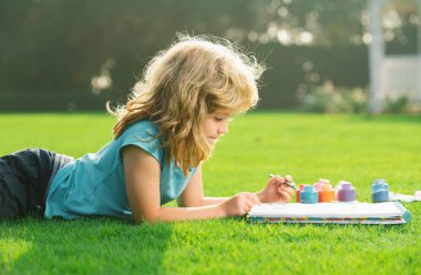 Çocuk resimleri. Çocuk parkta resim çiziyor, resim yapıyor. Küçük ressam açık havada resimler çizer.