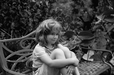 Çocuk bankta oturur. Dışarıdaki sevimli çocuğun hayat tarzı portresi. Yazlık çocukların açık hava portresi. Yazlık parkta oynayan yakın plan yüzlü çocuk. Çocuk güneşli bir yaz gününde dışarıda eğleniyor.