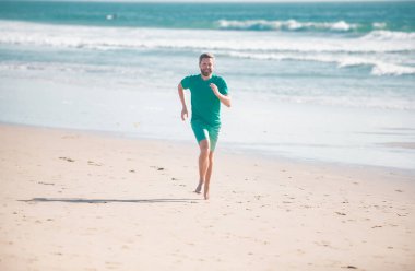 Adam kaçıyor. Erkek atlet kumsalda koşuyor.