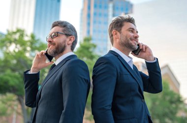 Şehirde akıllı telefon kullanan İspanyol iş adamları. Takım elbiseli yakışıklı işadamları cep telefonunu arıyor. Cep telefonu, ağ teknolojisi ve internet ile finans haberleri. İş başarılı konsept