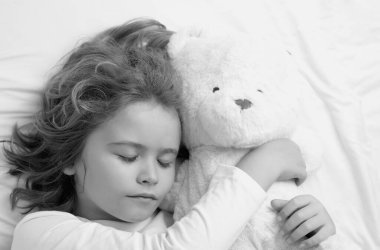 Sessiz bir uyku. Yatakta oyuncak ayıyla uyuyan bir çocuk. Yatma zamanı, çocuklar uyuyor. Çocuk yastıkta uyuyor, sağlıklı bir uyku çekiyor.