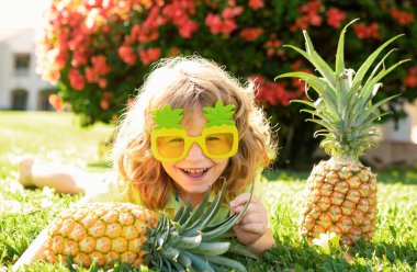 Kafasında ananas olan bir çocuk, taze tropikal meyvelerle oynuyor. Heyecanlı komik çocuk. Şaşkın bakışlı çocuk yüzü. Çocuklar yaz partisi