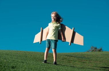 Oyuncak karton uçak kanatları olan komik çocuk. Başlangıç özgürlüğü konsepti. Havacı kostümü giyen bir çocuk. Küçük pilotun uçmayı hayal ettiğini